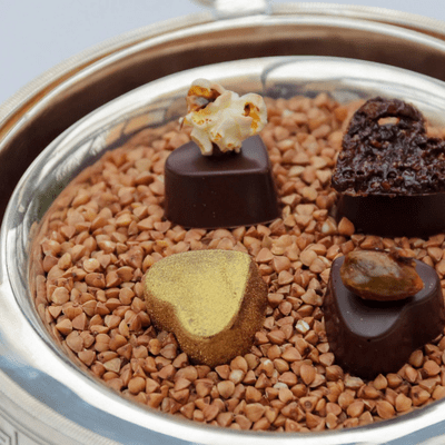Pralinés au chocolat en forme de cœur présentés sur un lit de sarrasin grillé.