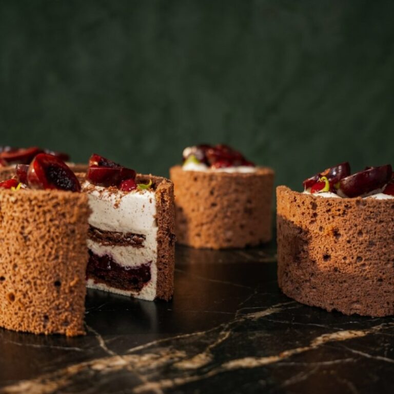 Petits gâteaux forêt noire à la vanille et au kirsch, garnis de crème et de cerises, sur un plan de travail en marbre.
